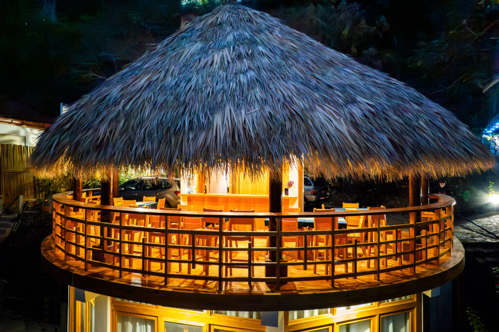 B'alam Ya Cafe outdoor seating area with a thatched roof at night.