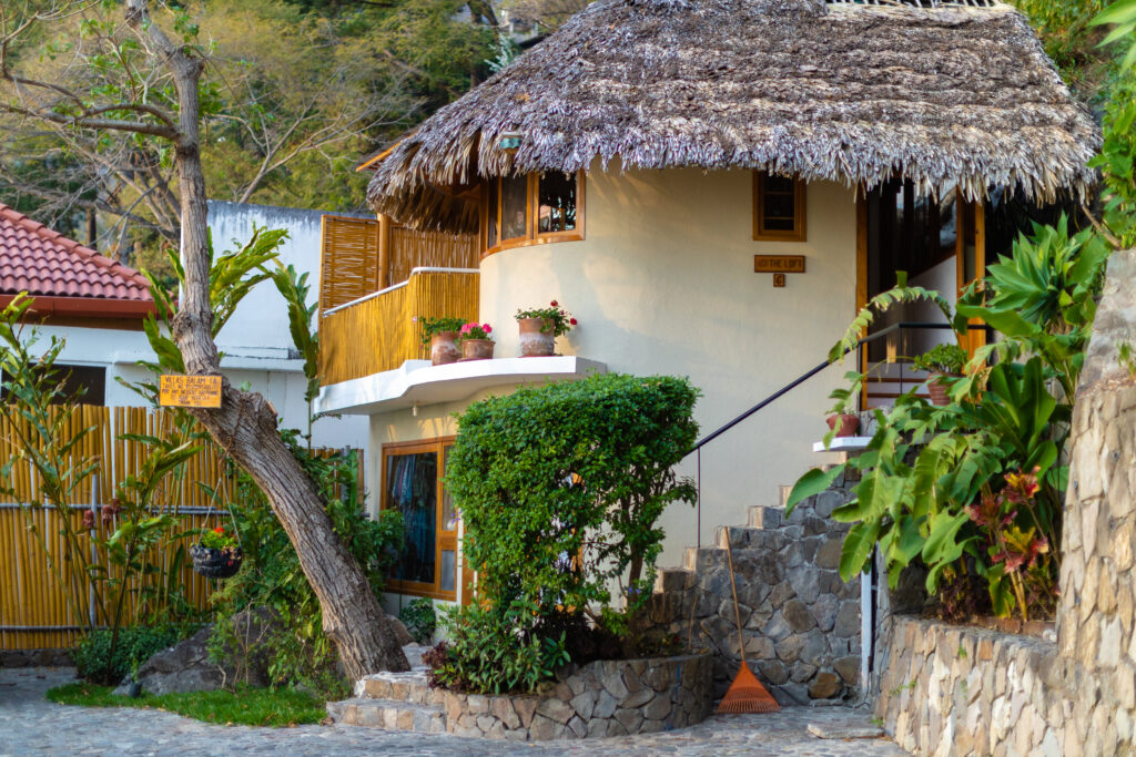 Villa Loft: Charming thatched-roof bungalow with stone stairs and lush greenery.
