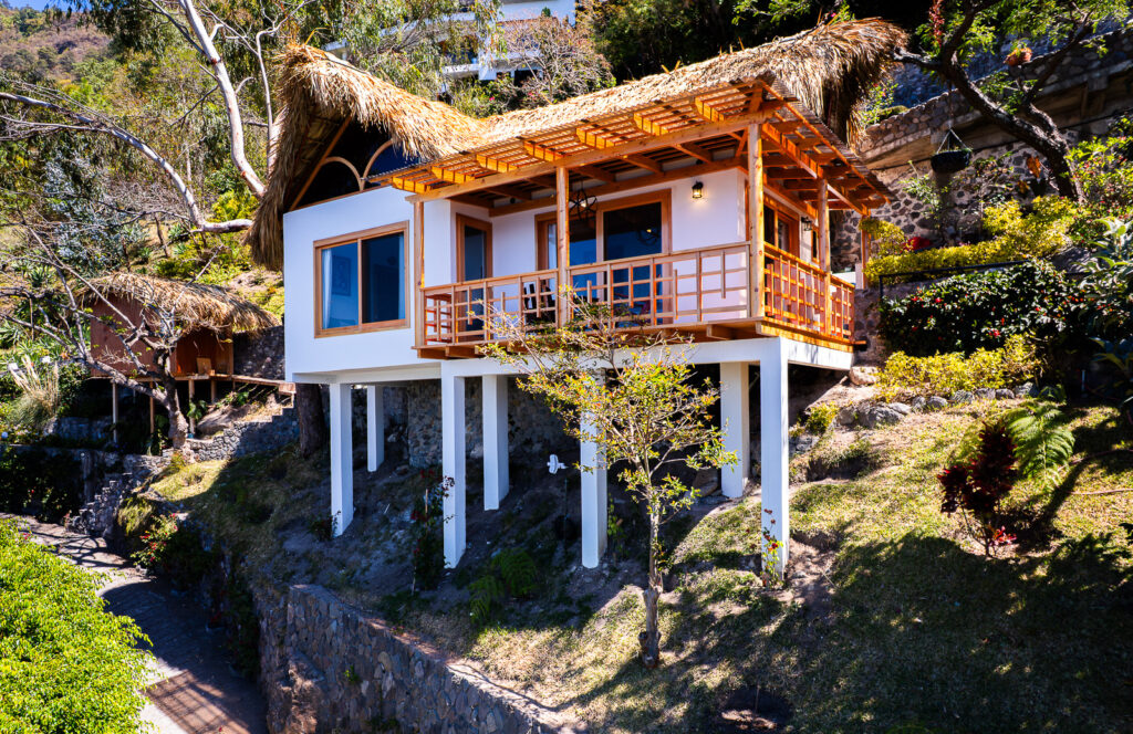 Villa Shakti: Elevated bungalow with thatched roof and wooden balcony on a lush hillside.